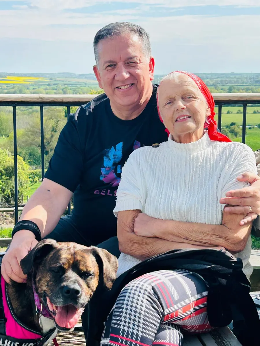 Linda smiling with a friend and a dog on a sunny terrace